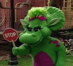 a green troll holding a stop sign in front of a red and white street sign