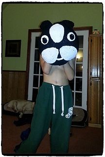 a man in green sweat pants holding up a black and white cat mask on his face