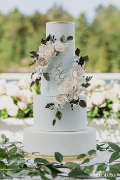 a wedding cake with white flowers on top and greenery around the bottom, sitting on a table