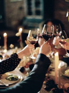 people are toasting with wine glasses at a dinner table