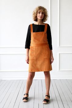 a woman wearing an orange apron and black top standing in front of a white wall