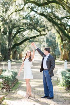 an engaged couple holding hands and walking down a path in front of trees with spanish moss