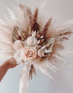 a bouquet with feathers and flowers in it being held by a person's hand