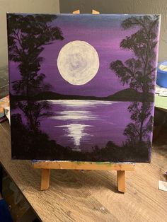 an easel with a painting on it that has a full moon in the sky