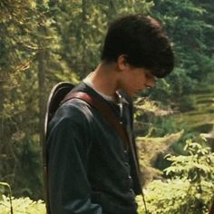 a young man standing in the woods looking down at his cell phone while wearing a backpack