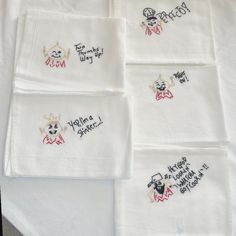 four embroidered napkins on top of a white table cloth with words written across them