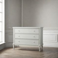 a white dresser sitting in the corner of a room next to a window with no curtains