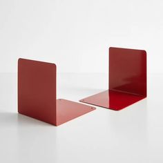 two red bookshelves sitting next to each other on a white surface with no one in the photo