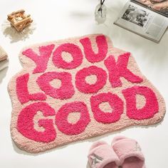 a pink rug with the words you look good written on it next to slippers