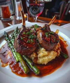 a white plate topped with meat and potatoes covered in gravy next to asparagus