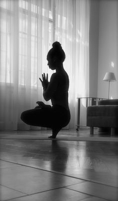 a woman sitting on the floor in front of a window with her hands clasped up