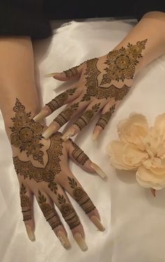 two hands with henna designs on them sitting next to a white flower and petals