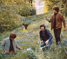 three people in a field with blue flowers and one person holding something up to the ground