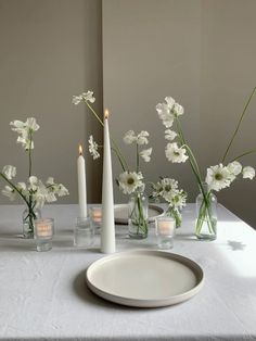 white flowers in vases and candles on a table with a plate, candle holders and plates