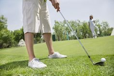 two people playing golf in the grass on a sunny day with one person about to hit the ball