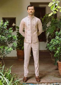 a man standing in front of potted plants wearing a beige suit and brown shoes