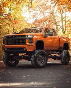 an orange truck parked on the side of a road in front of trees with leaves