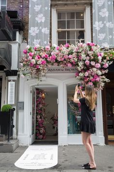 a woman taking a photo of flowers on the outside of a store front with her camera