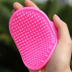 a hand holding a pink hair brush in front of a green plant with white dots