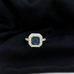 an emerald and diamond ring sitting on top of a black cloth with diamonds around it