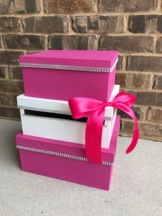 three boxes with pink ribbon and diamond trims on them, stacked against a brick wall