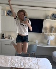 a woman jumping in the air with her cell phone up to her ear and wearing shorts