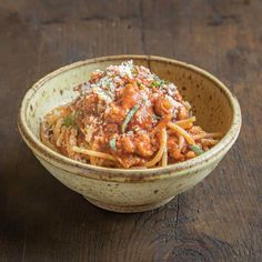 a bowl filled with pasta and meat covered in parmesan cheese on top of a wooden table