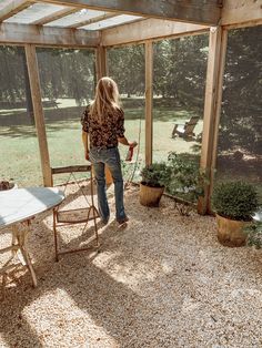 a woman is standing in the back yard looking at her bird feeder and some plants