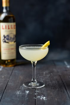 a glass filled with white liquid and a lemon wedge on the rim next to a bottle