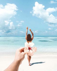 a person holding up a flower in front of the camera on a beach with blue sky and white clouds