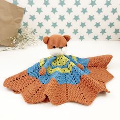 a crocheted teddy bear sitting on top of an orange and blue knitted blanket