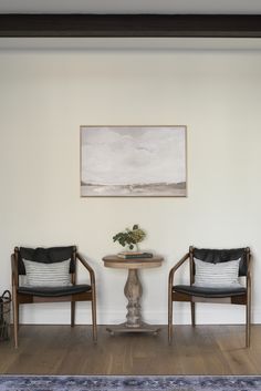 two chairs sitting next to each other in front of a table with a vase on it