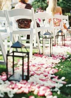 the aisle is lined with white chairs and pink petals on the grass, as well as lanterns