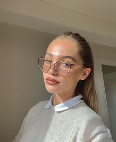 a woman wearing glasses and a white shirt is standing in front of a mirror looking at the camera