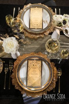 the table is set with gold and black plates, silverware, and white flowers