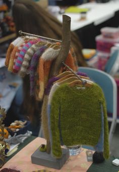 sweaters are hanging on a rack in a room with other items and people sitting at tables