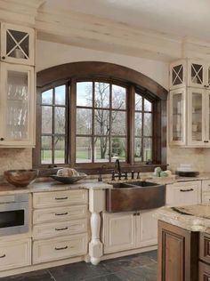 a large kitchen with marble counter tops and white cabinets, along with an arched window