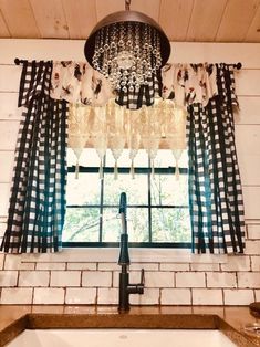 a kitchen sink under a chandelier in front of a window with black and white checkered curtains