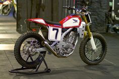 a red and white dirt bike parked on top of a sidewalk