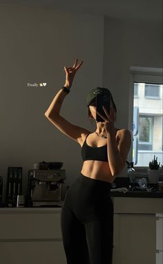 a woman in black sports bra top and leggings holding her hand up to the side