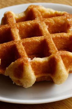 a waffle on a white plate sitting on a wooden table