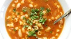 a white bowl filled with pasta soup and garnished with parsley