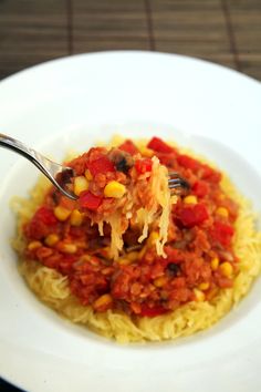 a spoonful of spaghetti with corn and tomato sauce over it on a white plate