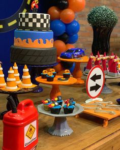 a table topped with cakes and cupcakes on top of wooden tables next to balloons