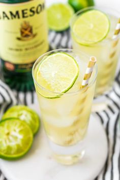 two glasses filled with lemonade and limes on a plate next to a bottle