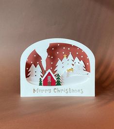 a merry christmas card with trees and houses in the snow, on a table top