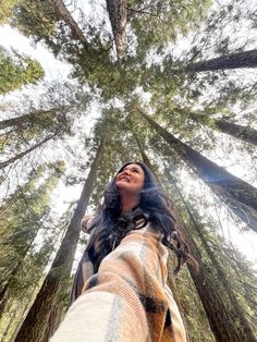 a woman standing in the middle of a forest looking up into the sky