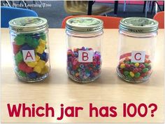 three jars filled with different types of candies on top of a wooden table next to a sign that says which jar has 100?