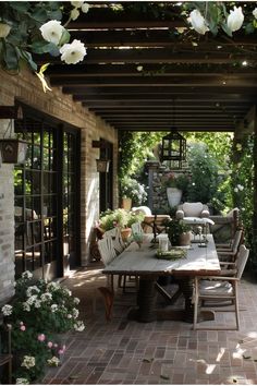 an outdoor dining area with white flowers and greenery on the roof, surrounded by brick walls