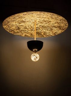 a light that is hanging from the ceiling in front of a black wall with gold foil on it